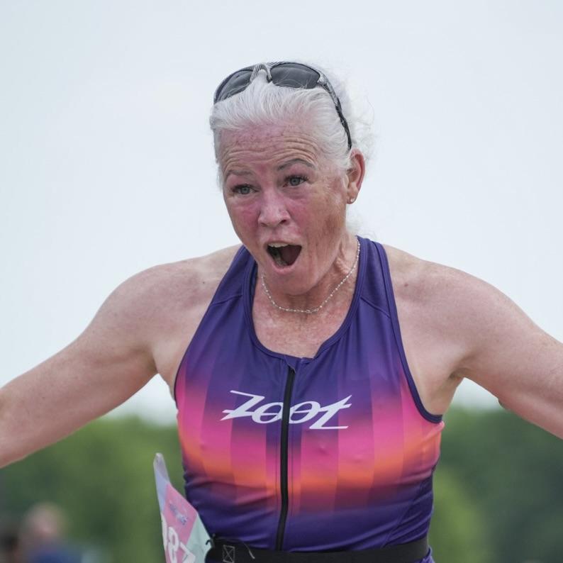 Chris at a triathlon finish line, arms wide, mouth open in celebration